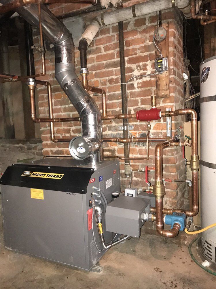 Basement boiler and ductwork against a brick wall with exposed pipes and a water heater.