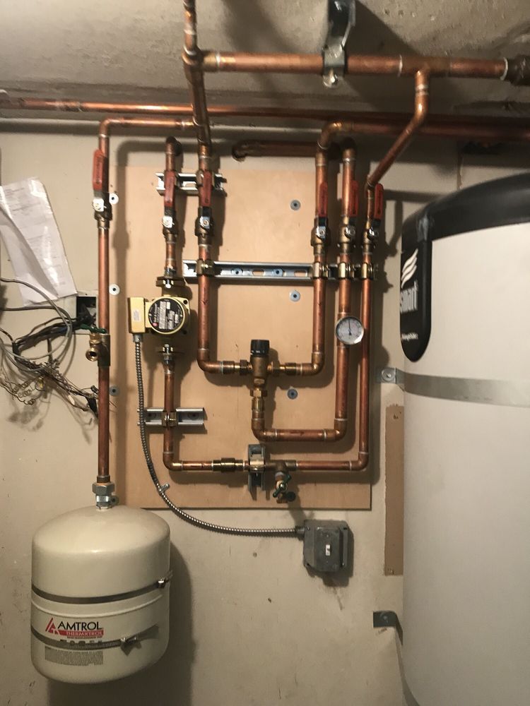 Copper plumbing pipes and valves mounted on a wall above a beige expansion tank in a utility room.