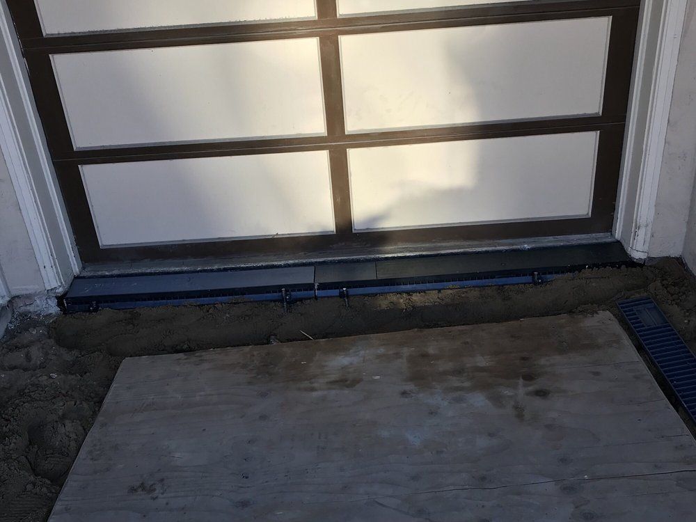 Garage threshold with worn concrete floor and dark blue door track at the bottom of a paneled garage door