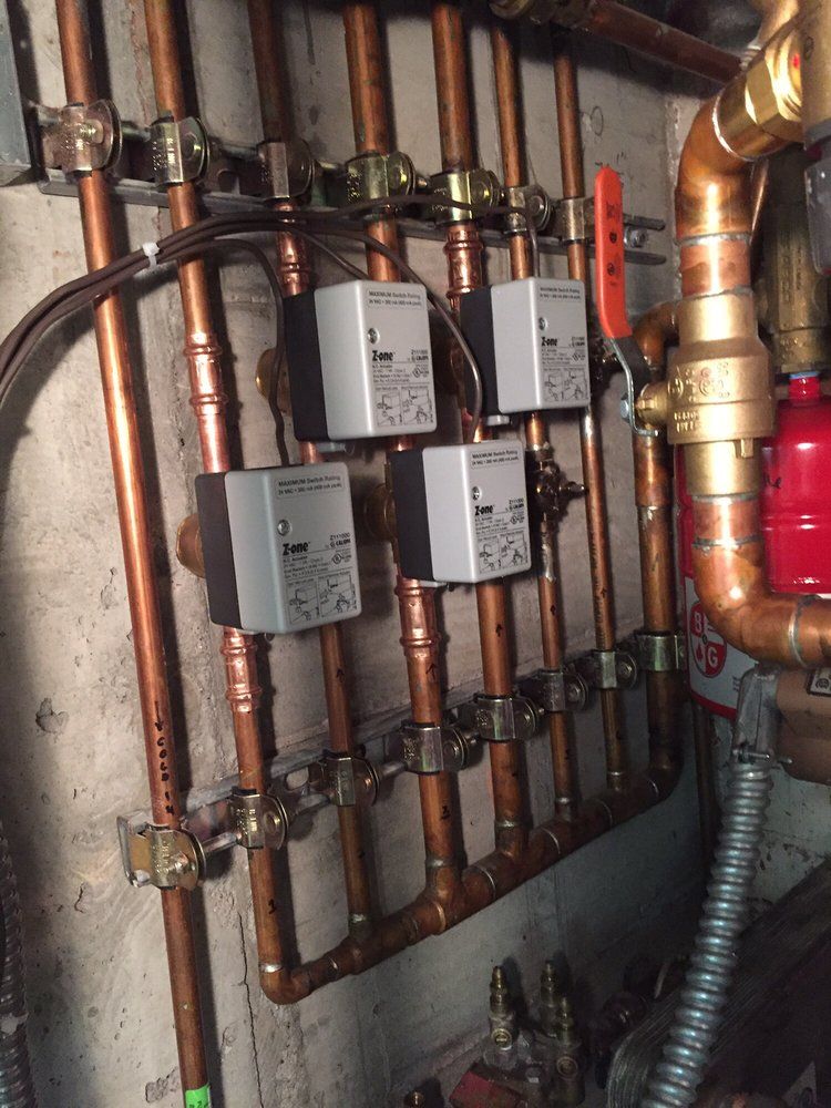 Copper plumbing manifold with gray valve controls and pipes in a utility room.