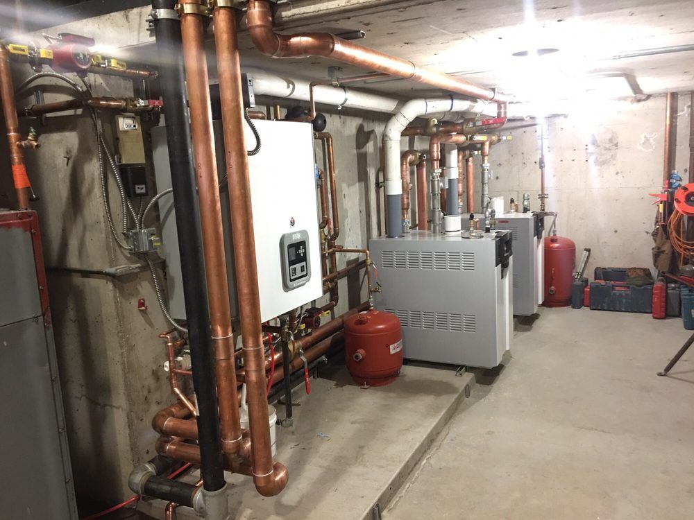 Basement utility room with copper pipes, boilers, and water tanks along a concrete wall