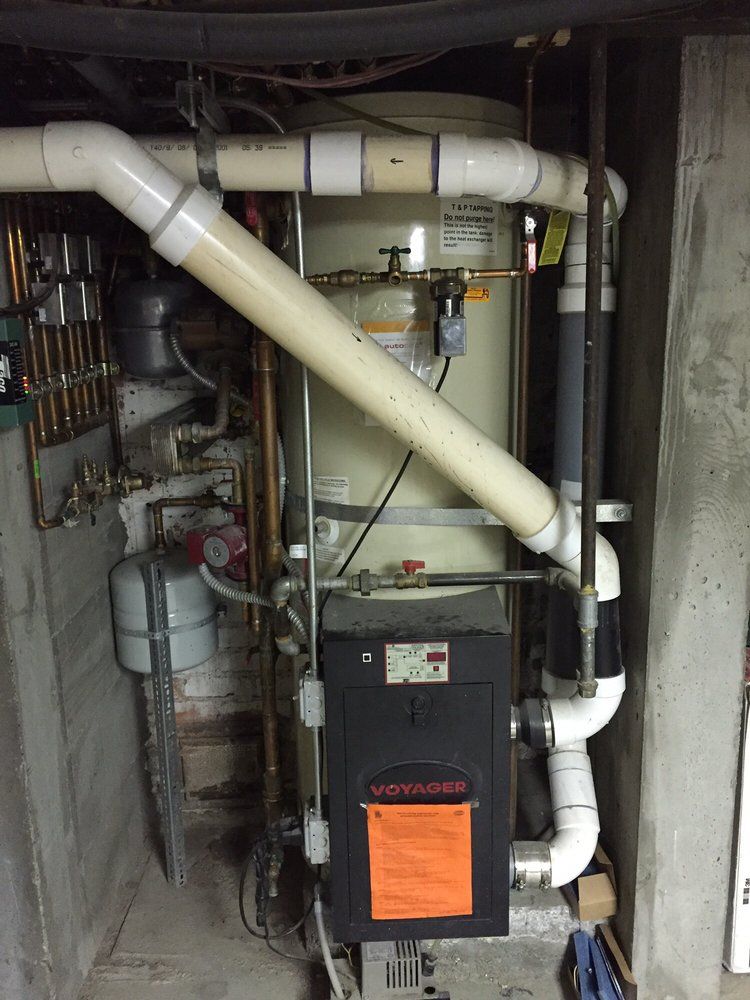 Compact furnace and HVAC ductwork in a utility closet, with white pipes and a black front panel.