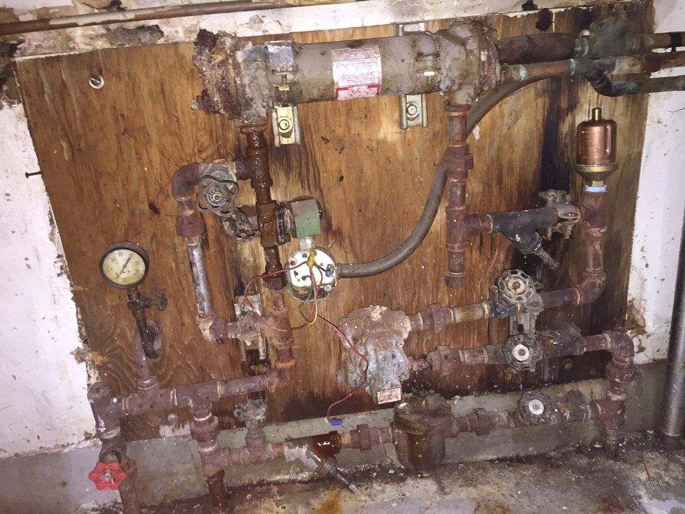 Rusty industrial pipes and valves mounted on a wooden wall with a pressure gauge.