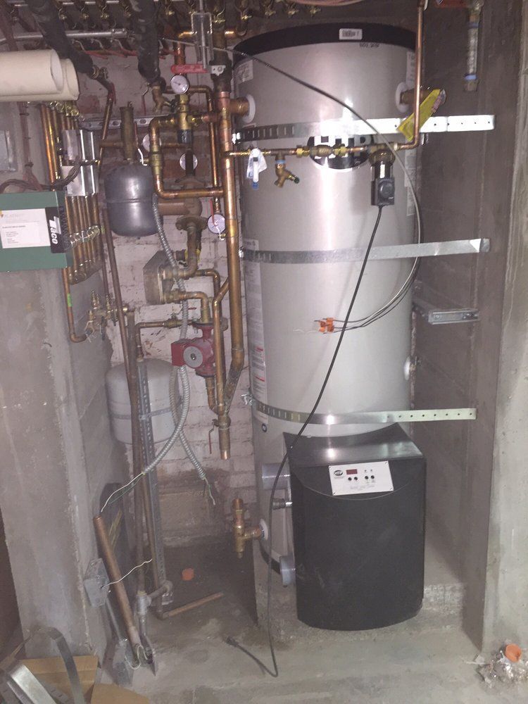 Water heater and plumbing equipment in a utility closet, with pipes, valves, and a black storage tank.