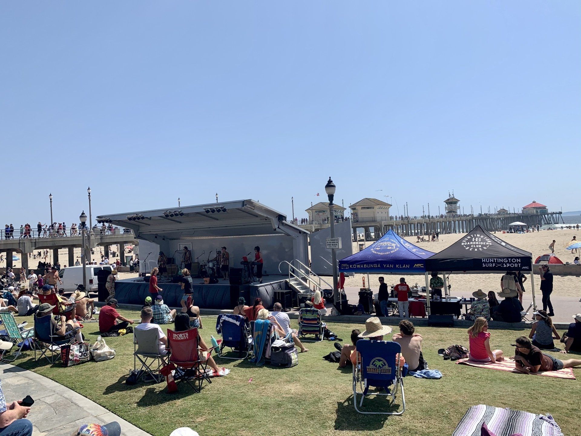 A group of people are sitting on the grass in front of a stage.