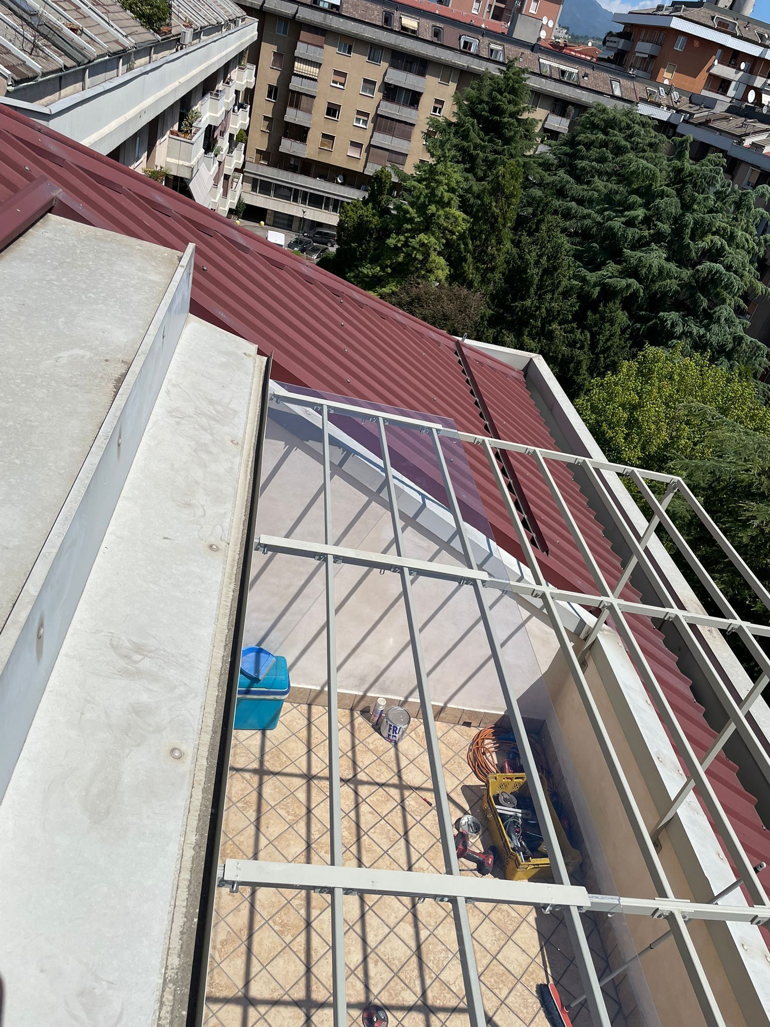 Vista dal tetto con ringhiera in metallo, tenda da sole rossa e palazzi della città sottostanti.