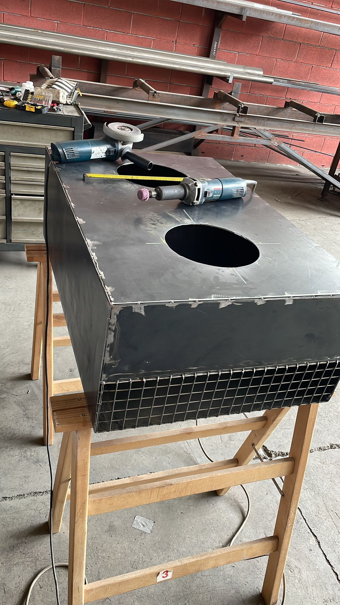 Scatola di metallo nero con un grande foro circolare, appoggiata su un supporto di legno in un'officina.