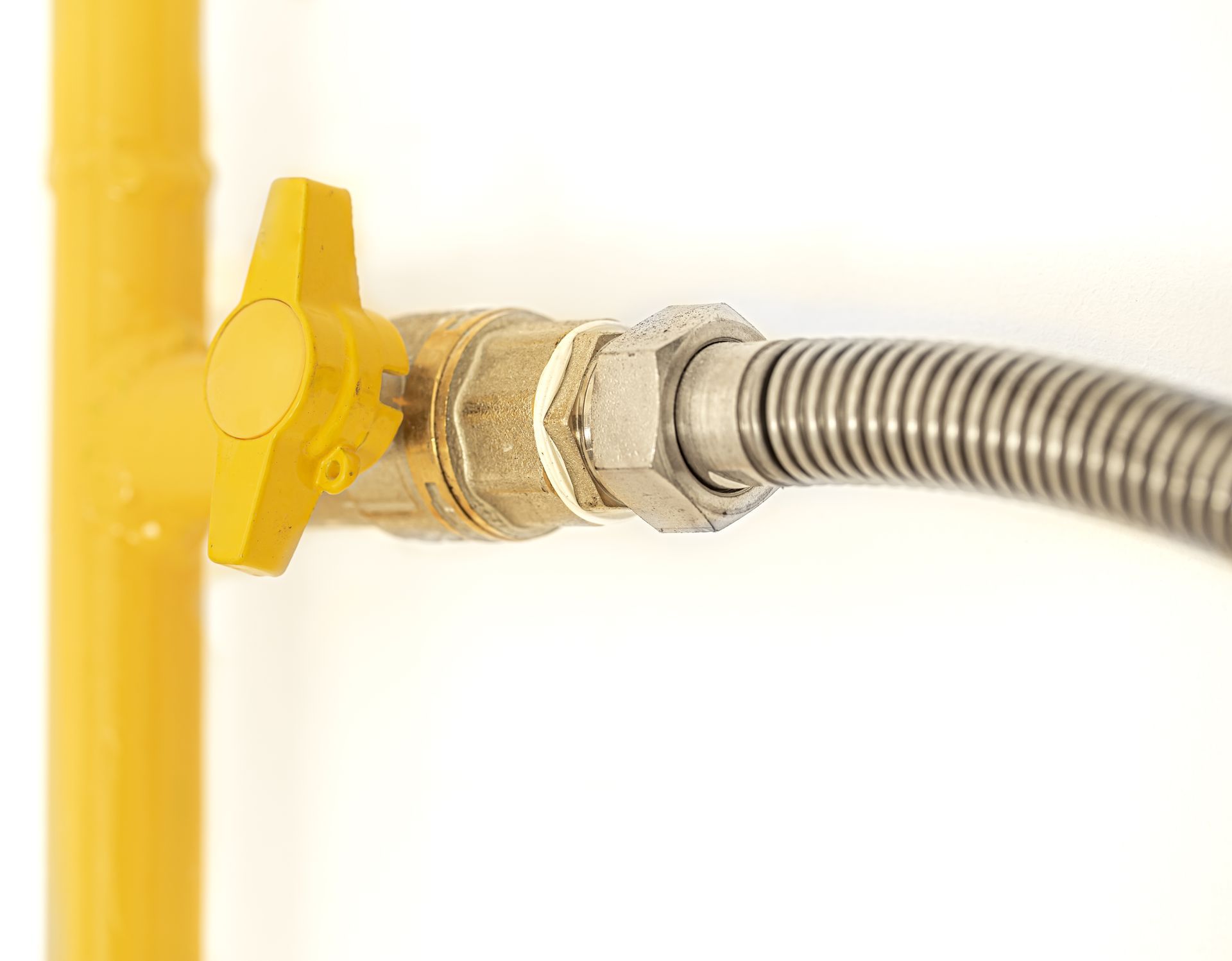 Yellow gas valve connected to a flexible metal hose on a yellow pipe.
