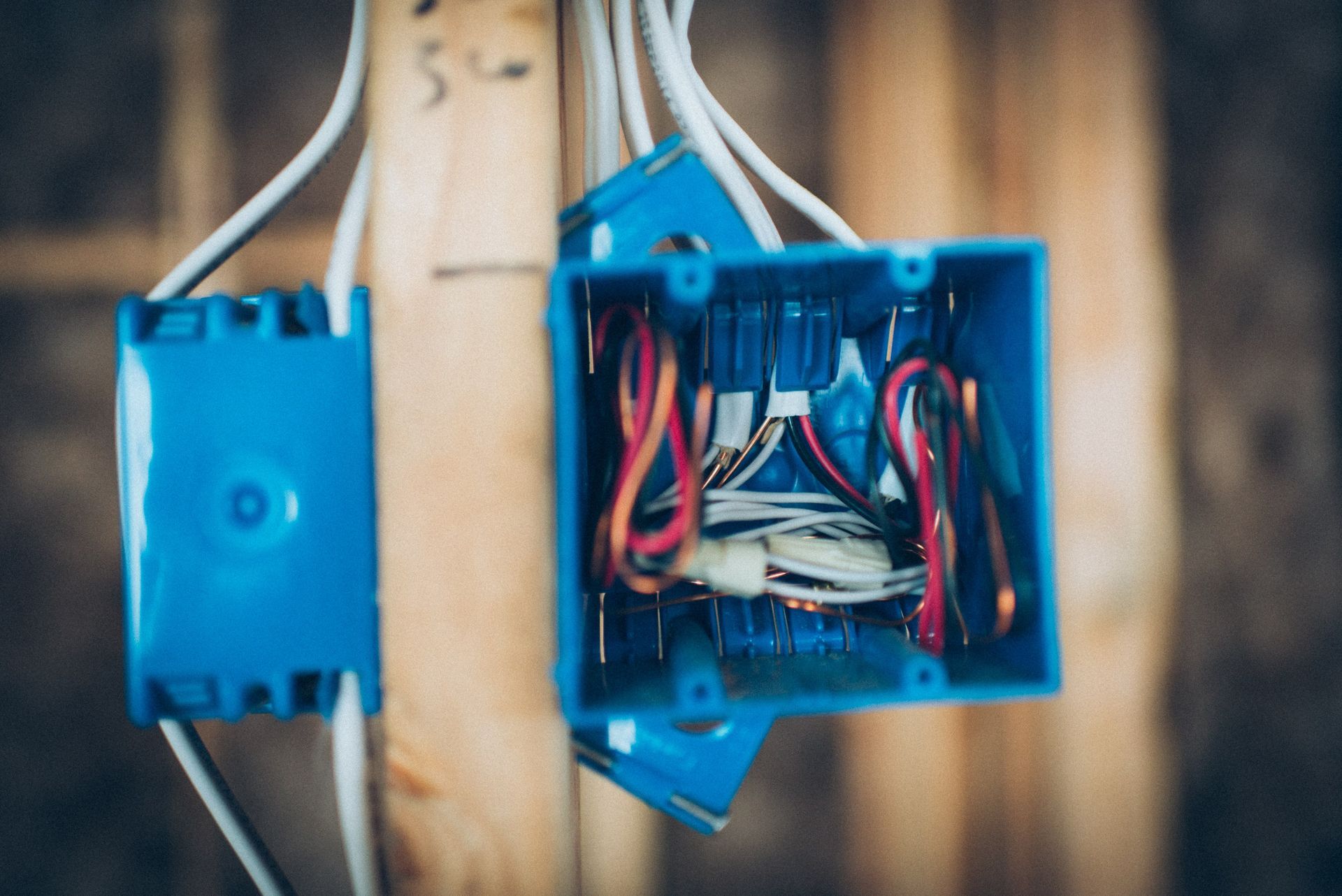 Blue electrical boxes with wires on wooden studs.