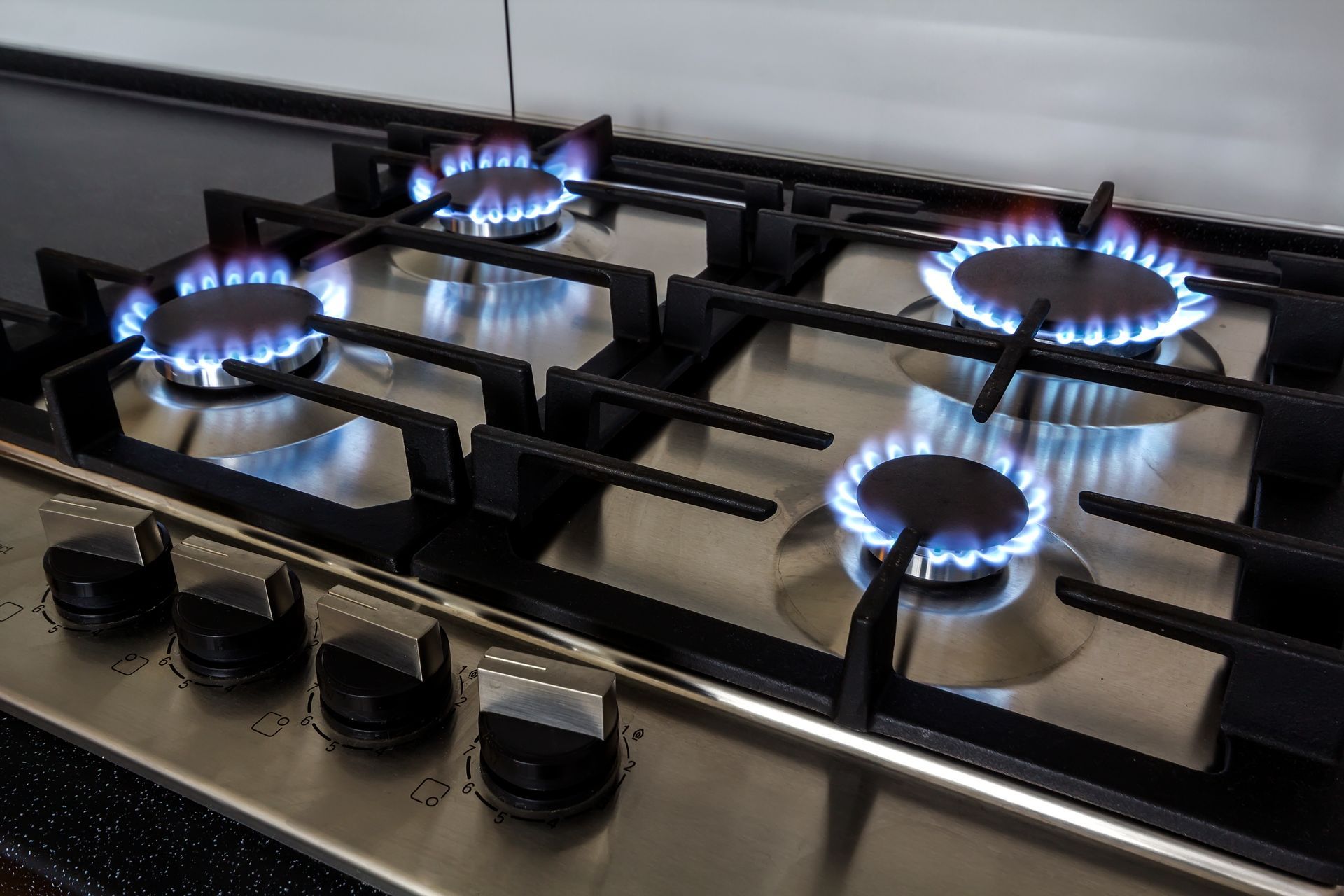 Gas stovetop with four blue flames burning brightly.