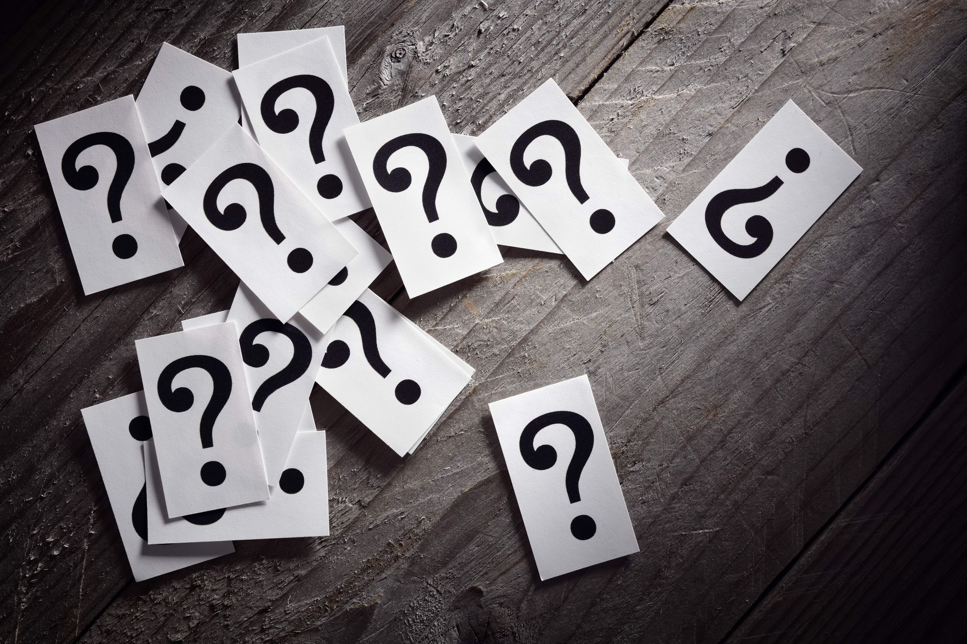 Scattered white cards with black question marks on a wooden surface.