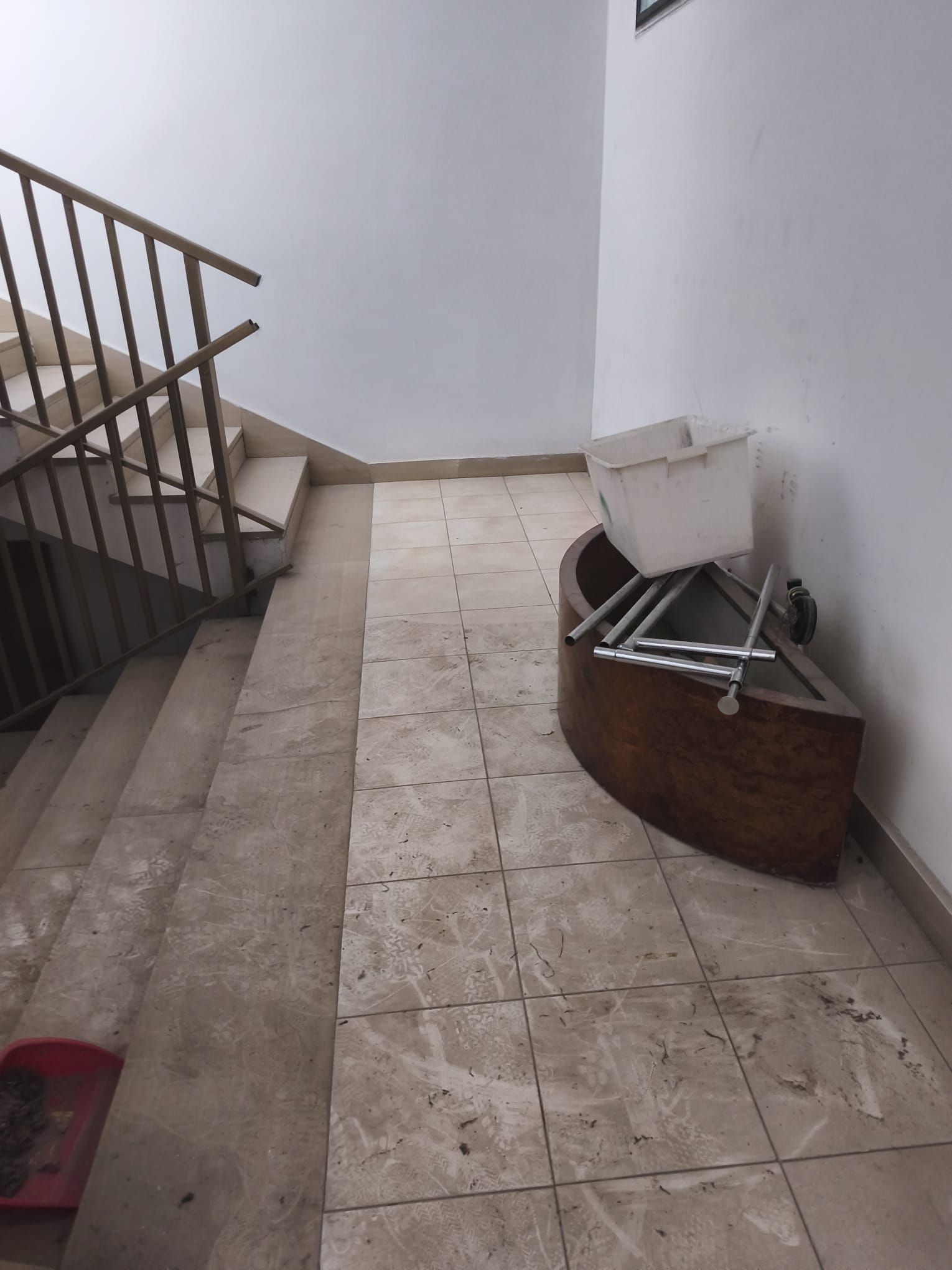 Vano scale interno con pareti bianche, pavimento piastrellato e una sedia rovesciata accanto al corrimano.