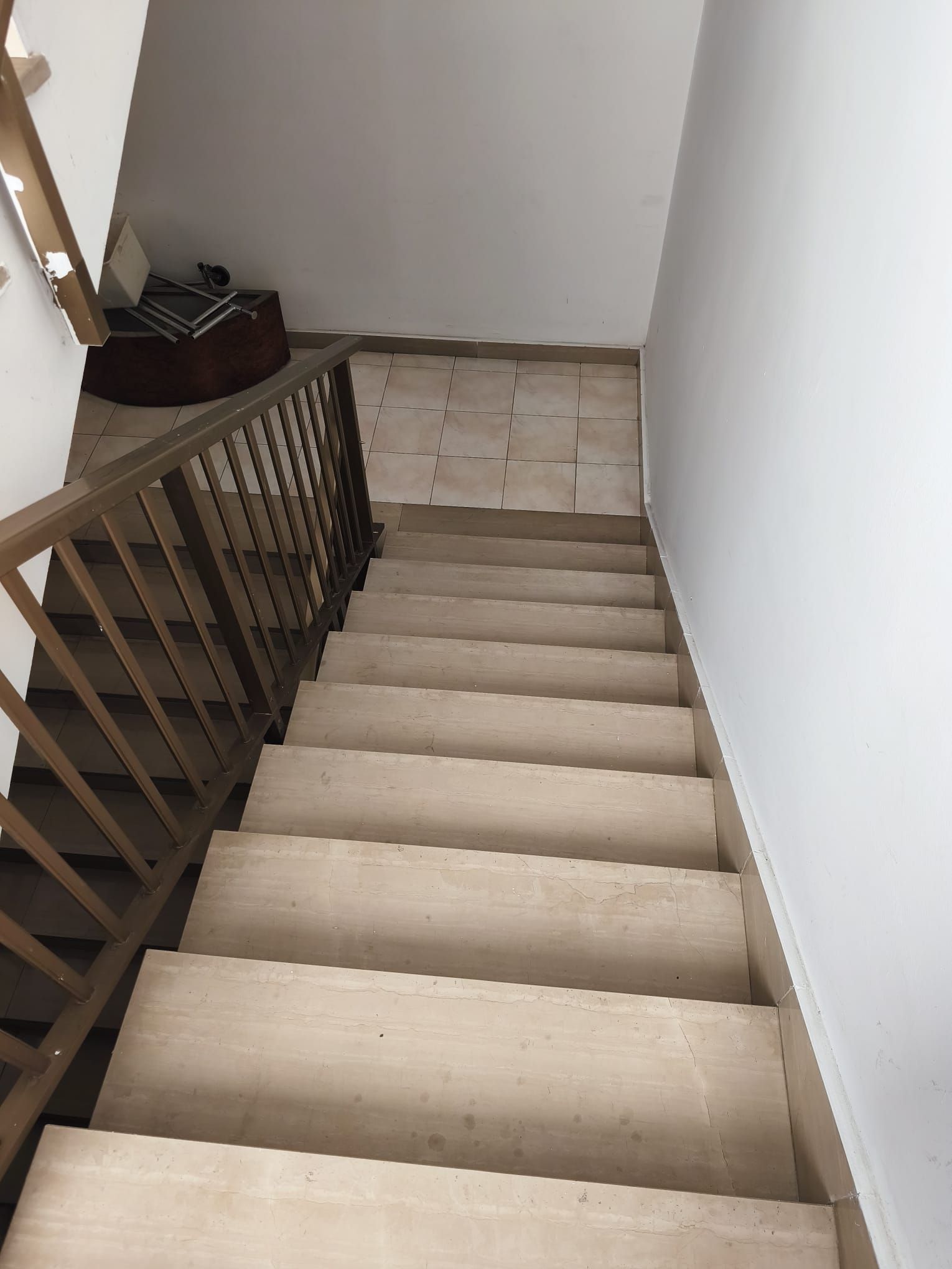 Scala interna vista dall'alto, con gradini rivestiti di moquette beige, pareti bianche e ringhiera in legno sulla sinistra.