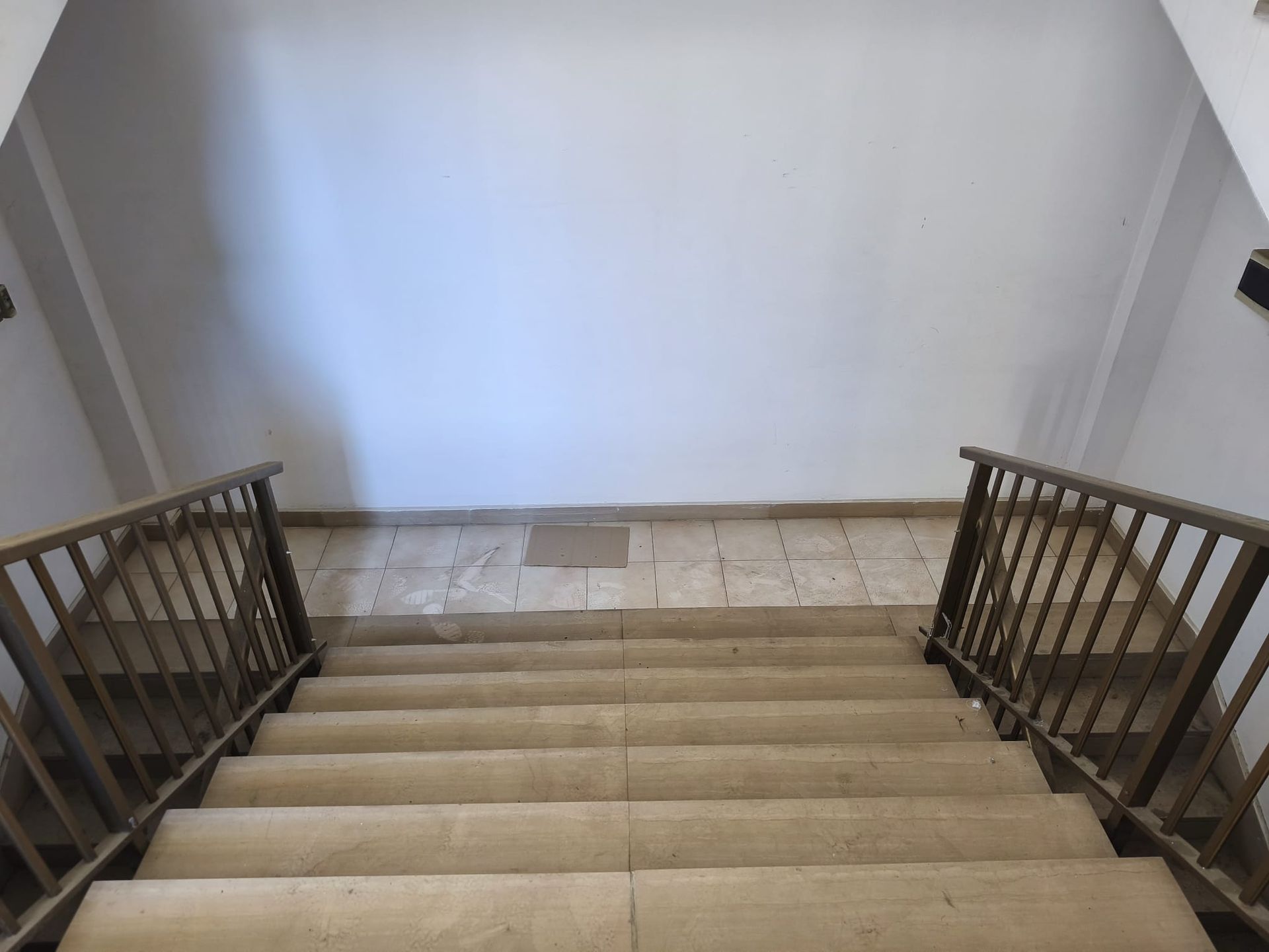 Parte superiore di una tromba delle scale rivestita di moquette con ringhiere in legno e pianerottolo piastrellato sottostante.