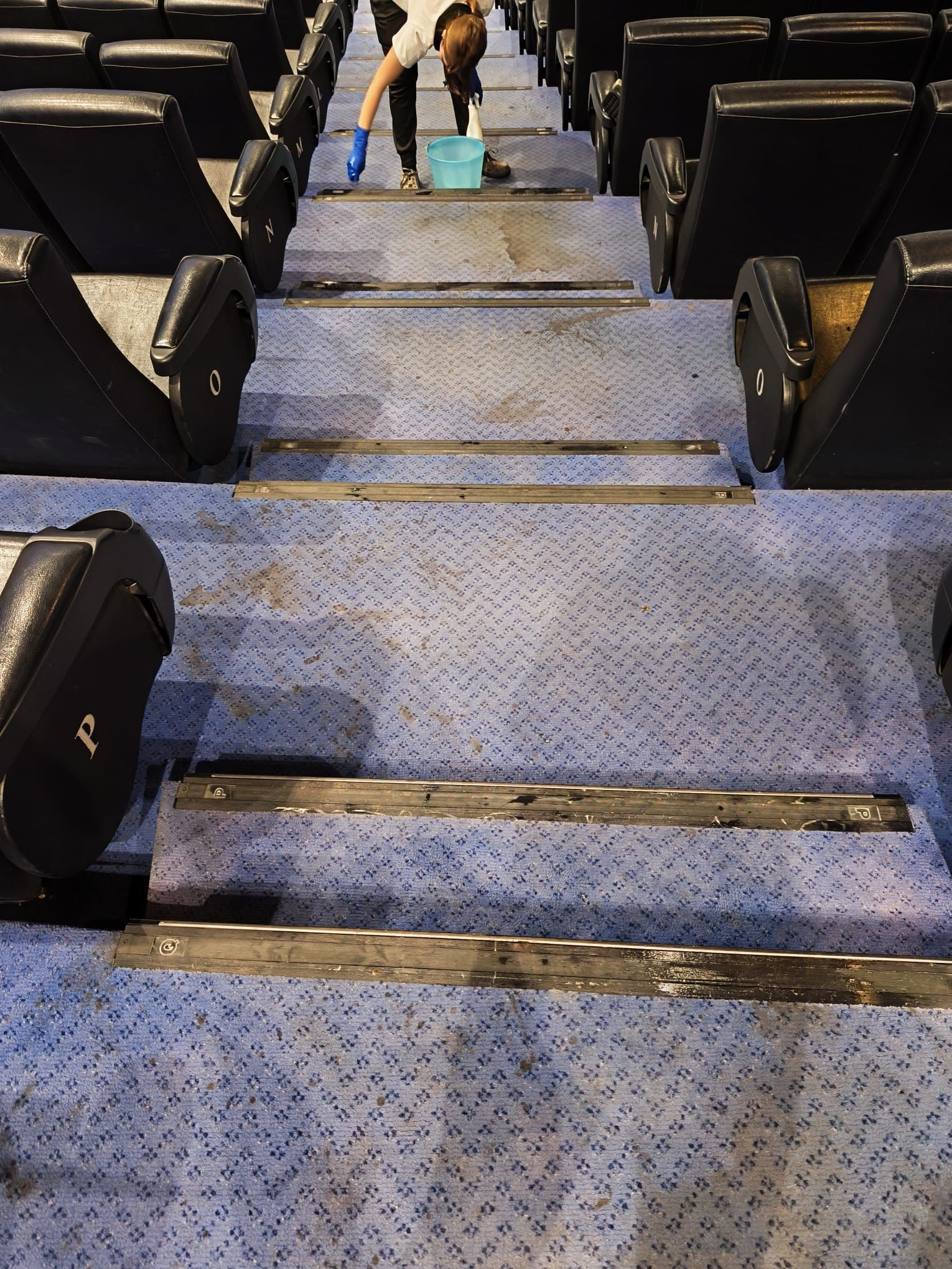Scale dell'auditorium ricoperte di moquette blu con braccioli neri, viste dal fondo verso il palcoscenico.
