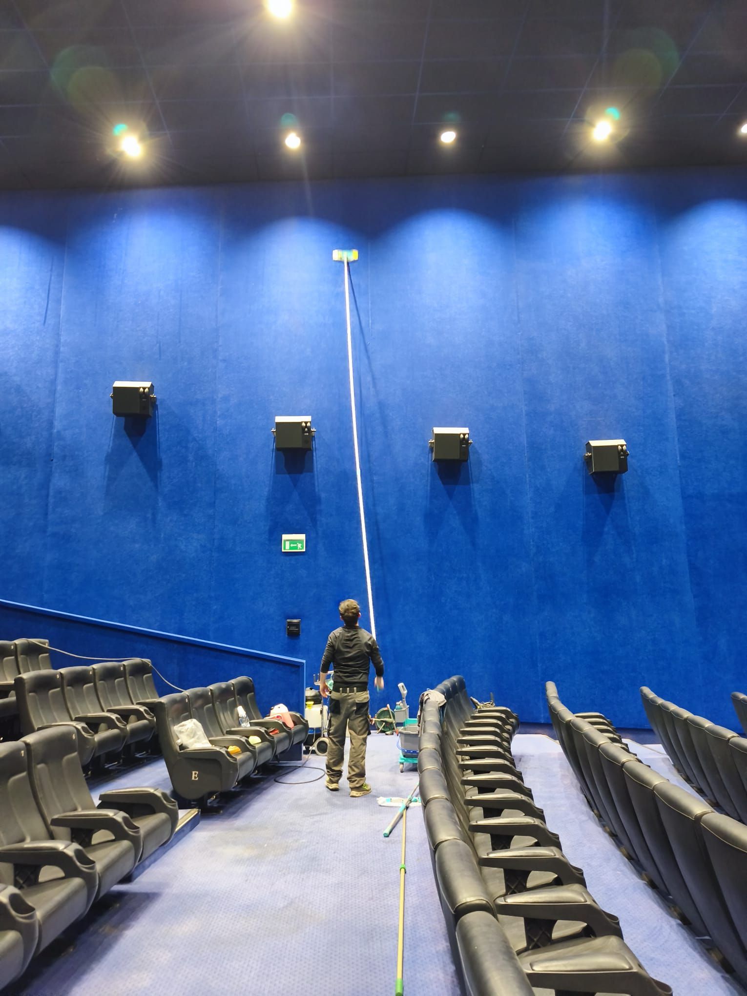 Due operai in un auditorium blu, uno dei quali su una piattaforma elevatrice intento a regolare un cavo vicino alle file di poltrone del teatro.