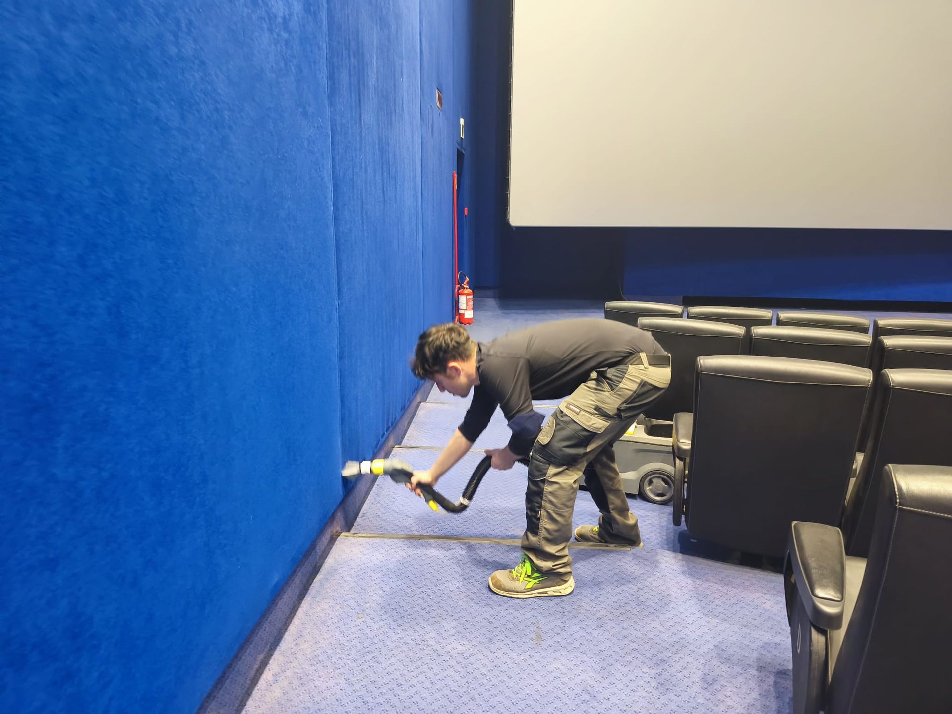 Una persona si protende verso una parete in un auditorium dalle pareti blu, accanto a file di sedie nere.