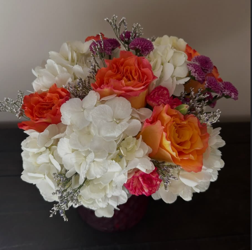 Colorful bouquet of white, orange, pink, and purple flowers in a dark vase on a black table