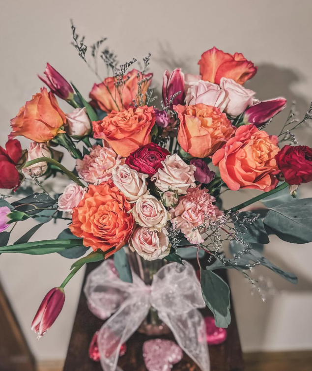 Bouquet of coral, pink, and white roses in a clear vase with a silver ribbon