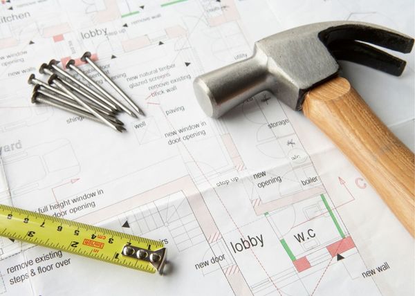 Handymen Nanaimo tools resting on home plans for renovations including a hammer, nails and a tape measure.