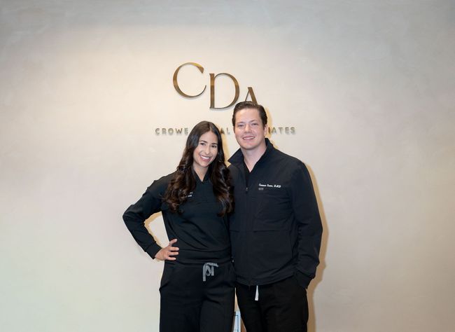 Two people standing and smiling in front of a CDA sign indoors.