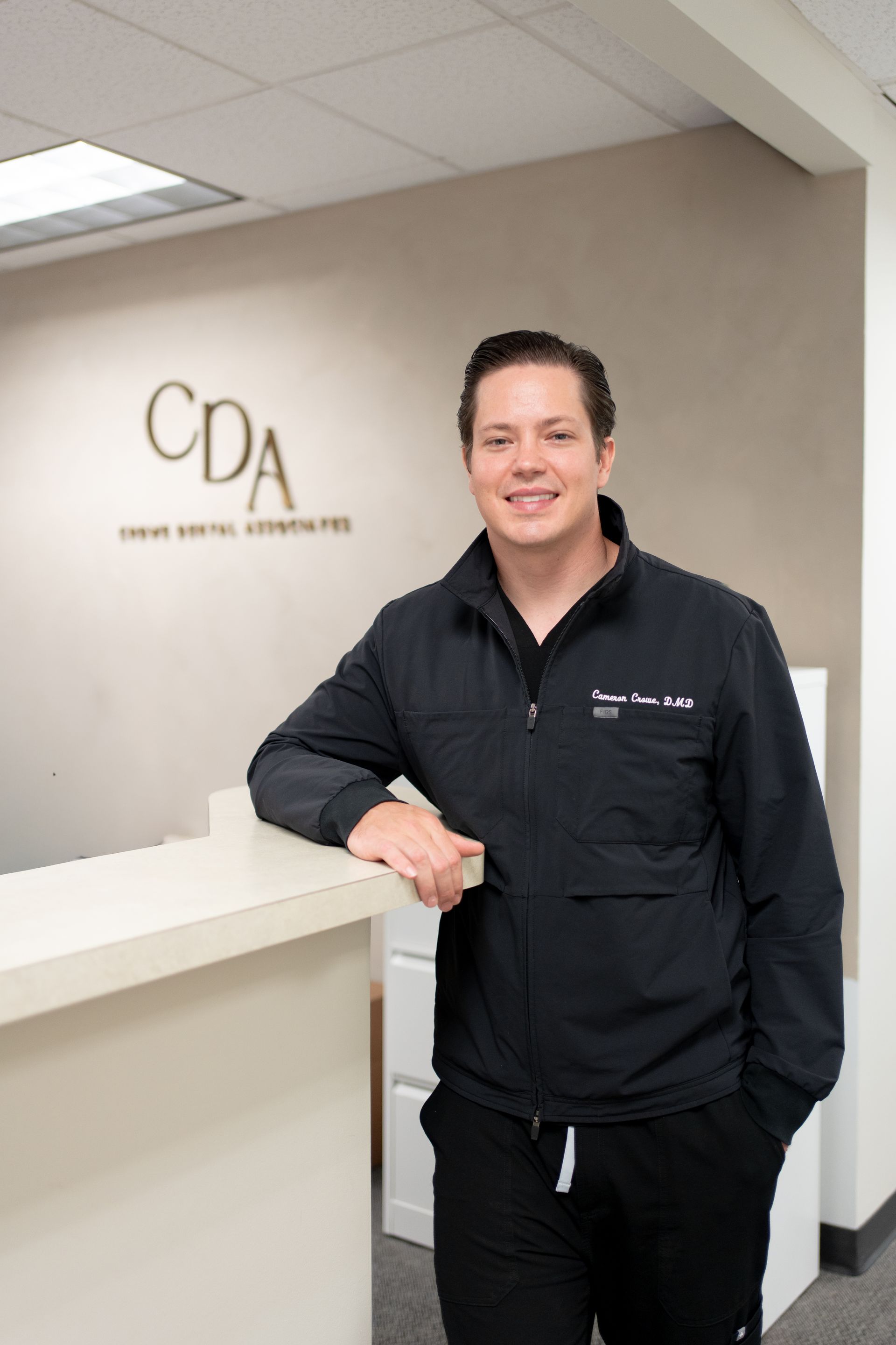 Person standing at a reception desk in a clinic lobby with a CDA logo on the wall.