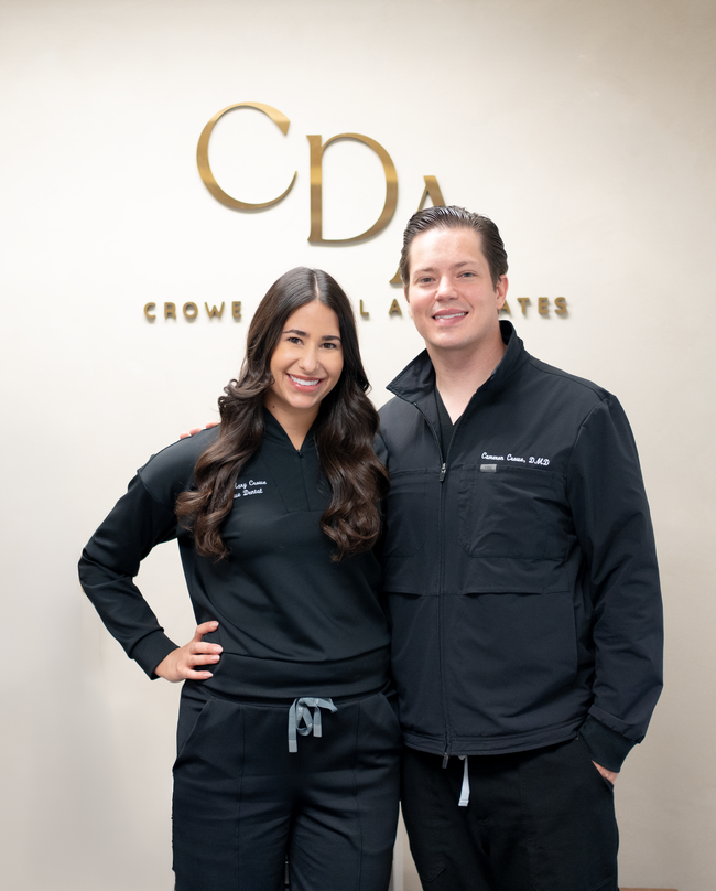 Two people standing and smiling in front of a CDA sign indoors.
