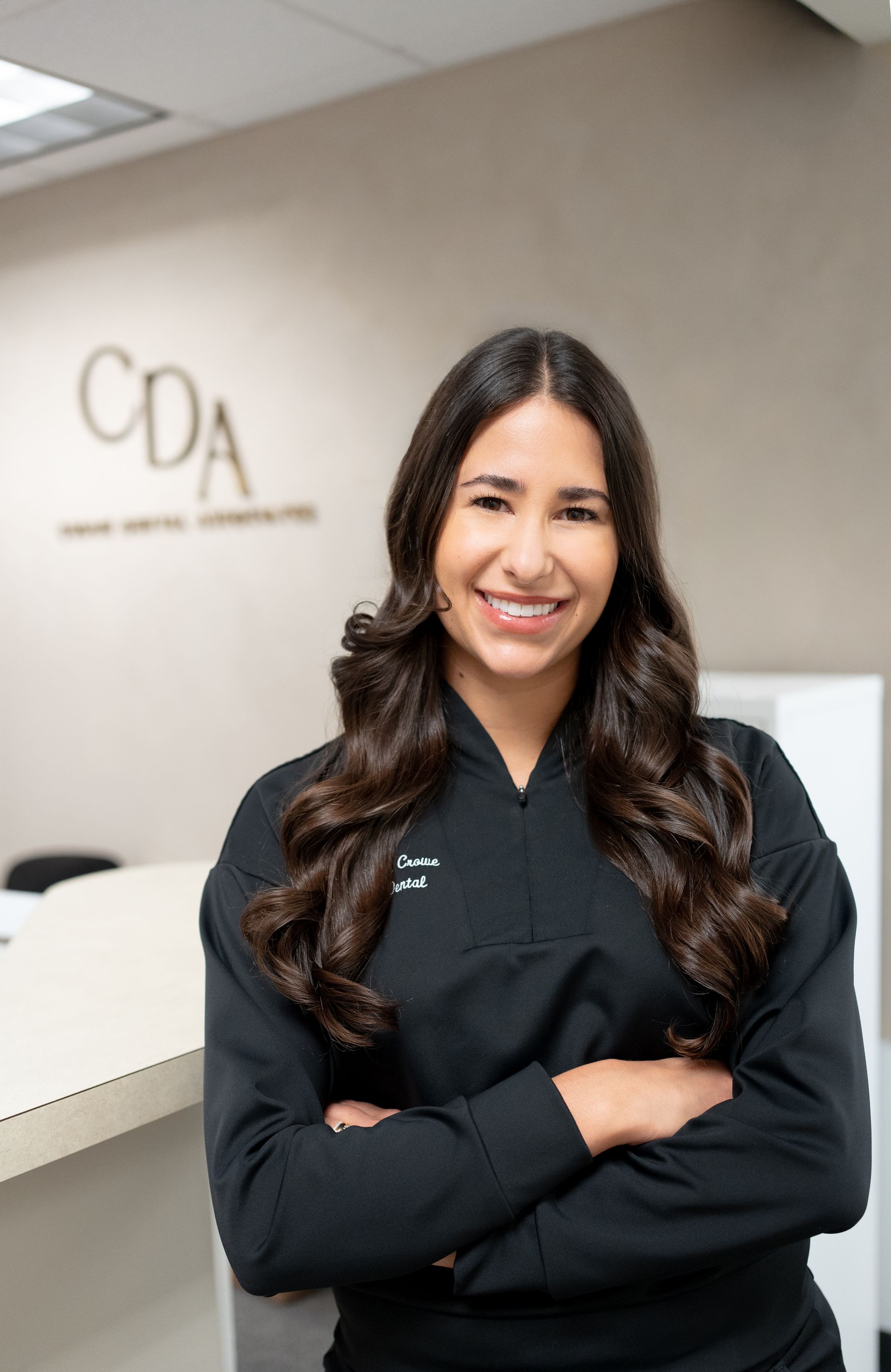 Smiling woman with arms crossed standing in a clinic lobby with a CDA sign behind her