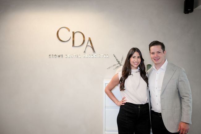 Two people standing in front of a CPA office sign, smiling at the camera.