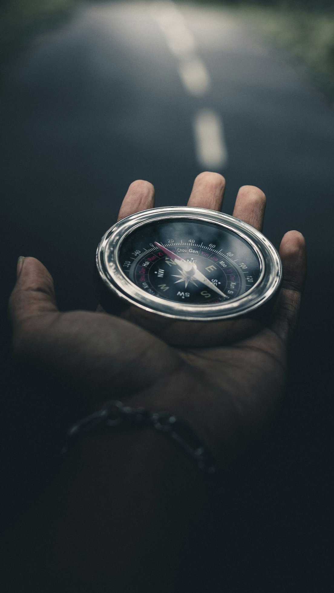 Mão segurando uma bússola; estrada ao fundo.