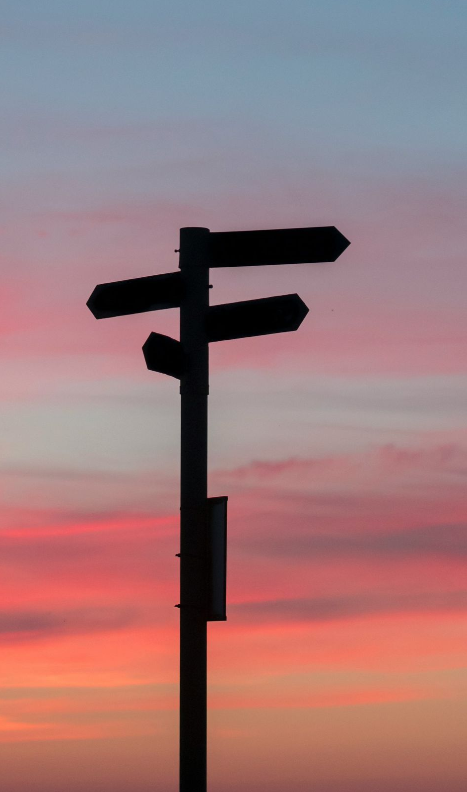 Silhueta de uma placa de sinalização com três indicações contra um céu colorido ao pôr do sol.