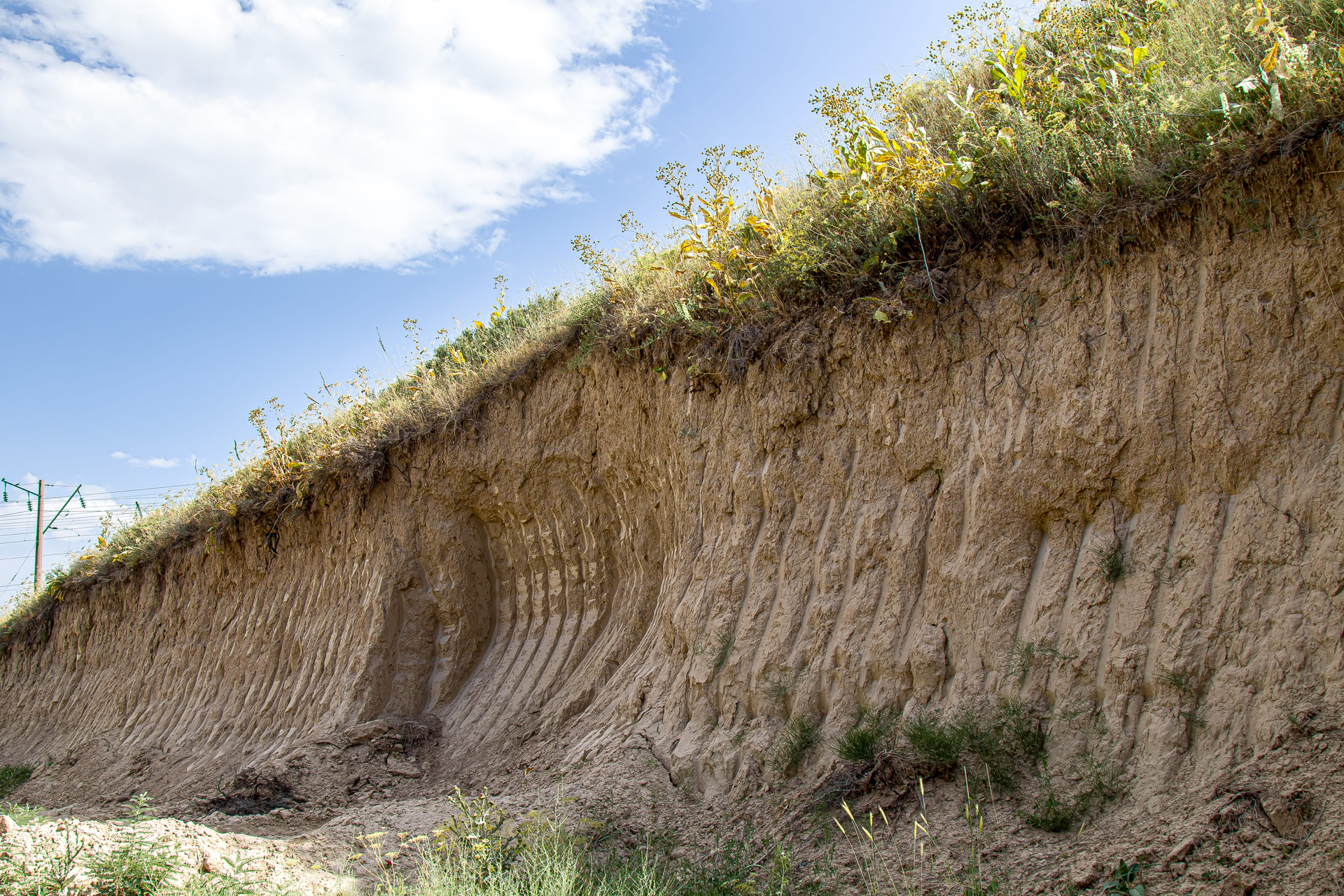 Steep dirt embankment with grass on top under a partly cloudy blue sky.