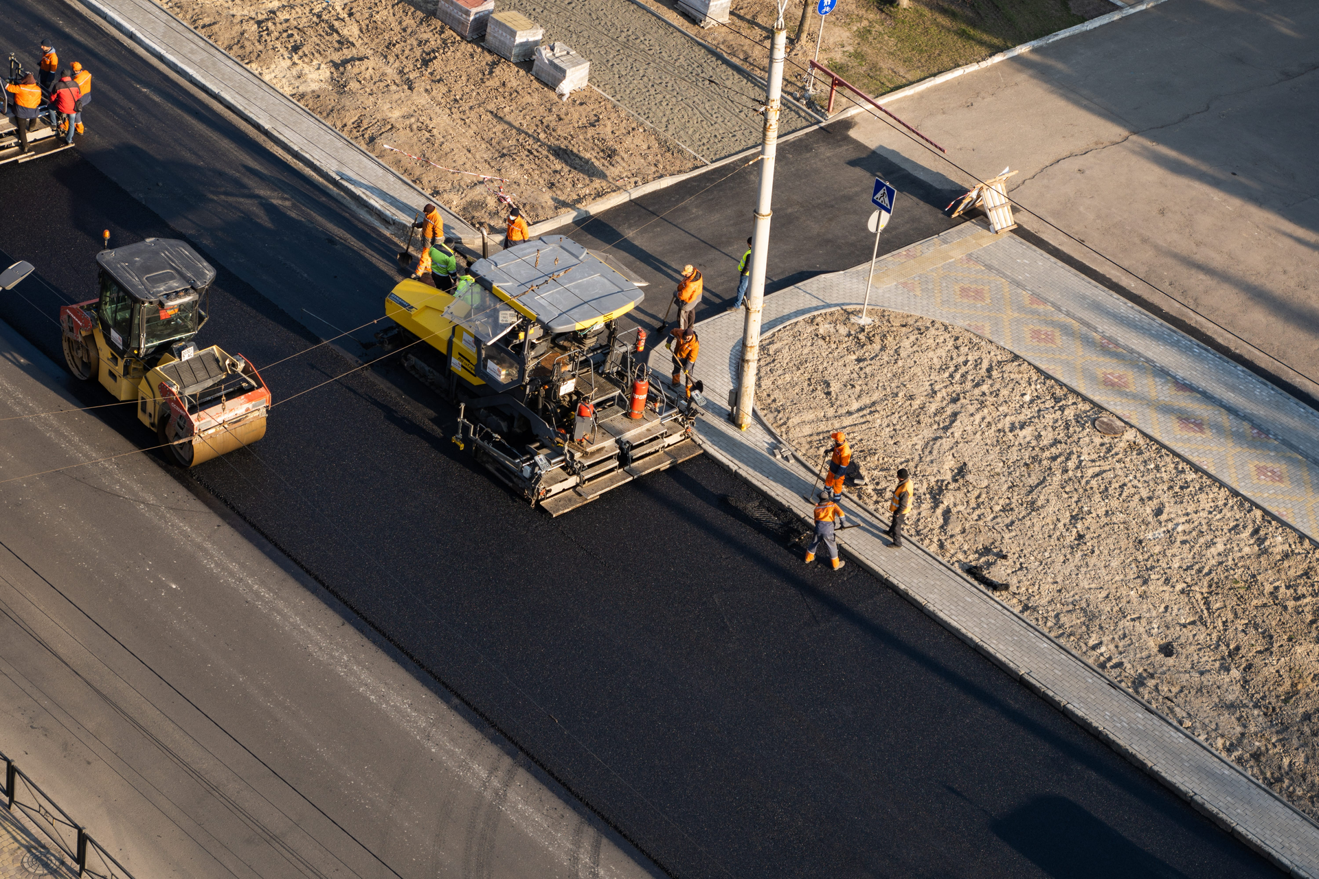 Road paving crew working with asphalt machines on a roadway beside a gravel shoulder