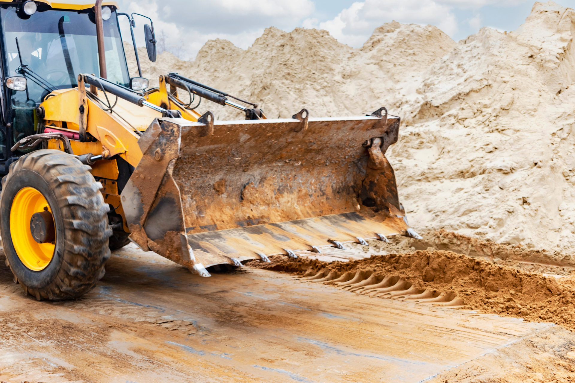 Yellow front loader pushing dirt in a sandy construction site