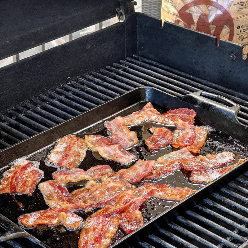 Bacon cooking in pan on grill with bag of Western Maple chips in background