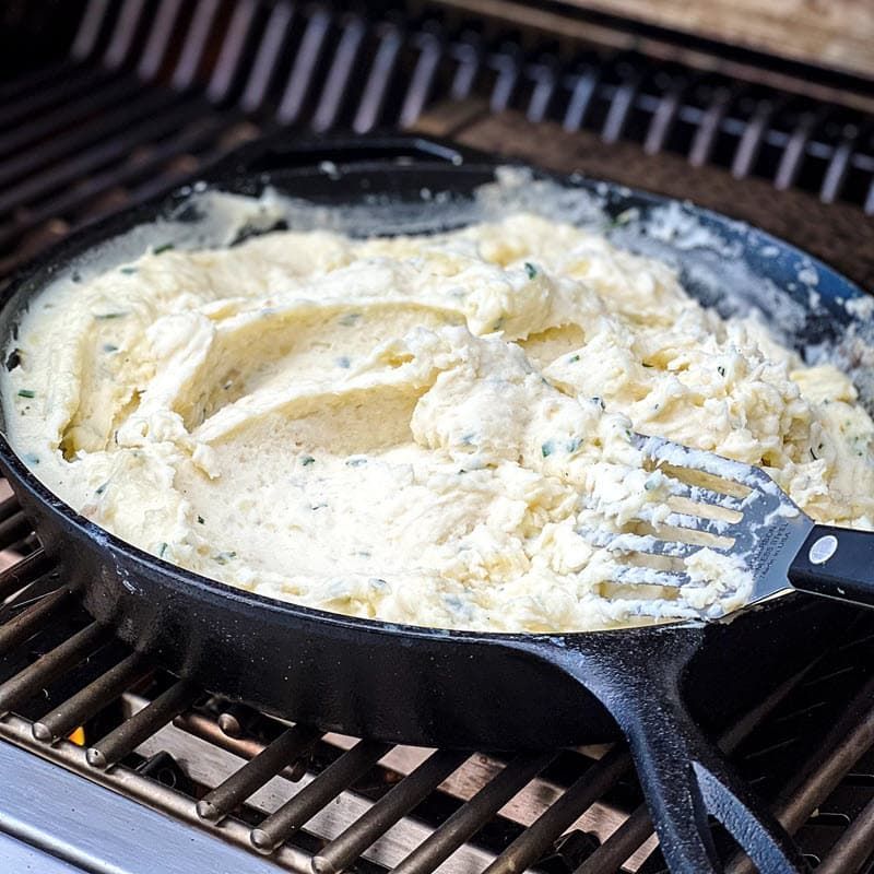 mashed potatoes with chives mixed in cast iron pan on grill