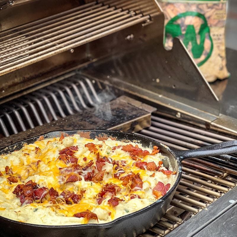Mashed potatoes with cheese, chives and bacon in cast iron pan and smoking chips box smoking on gas grill
