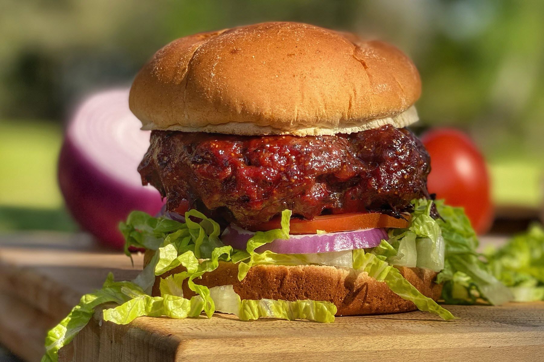 Juicy burger with lettuce and tomato with red onions and tomatoes in the background