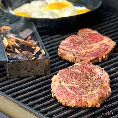 Steaks on grill, eggs cooking in cast iron pan and wood chips smoking in smokebox