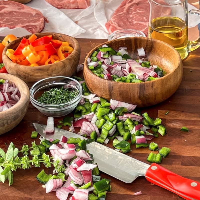 Raw steaks, peppers, basil, onion, olive oil and knife on cutting board