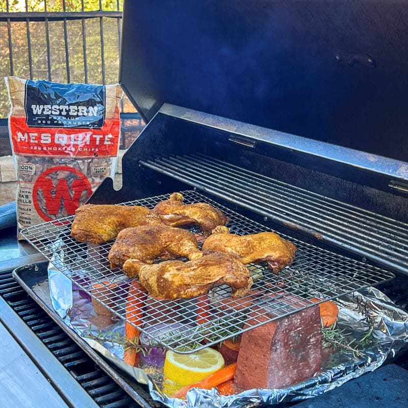 Chicken Legs and veggies on the grill with a bag of Western Mesquite BBQ Smoking Chips in background