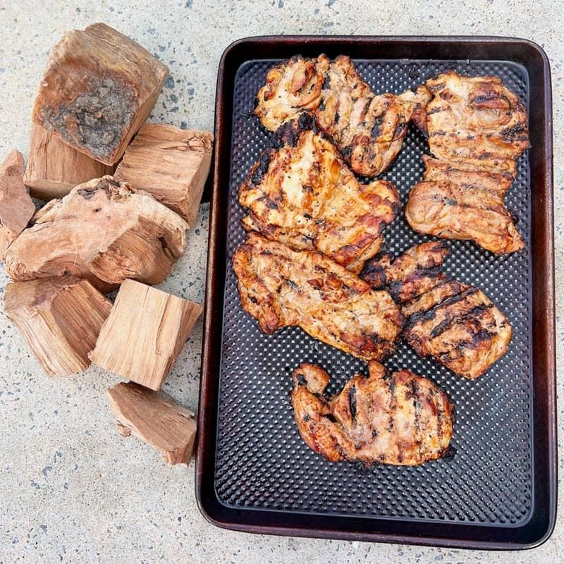 Western raw cherry wood chunks next to pan of grilled chicken thighs