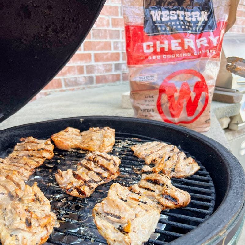chicken thighs on the grill with bag of Western Cherry Wood chunks in background