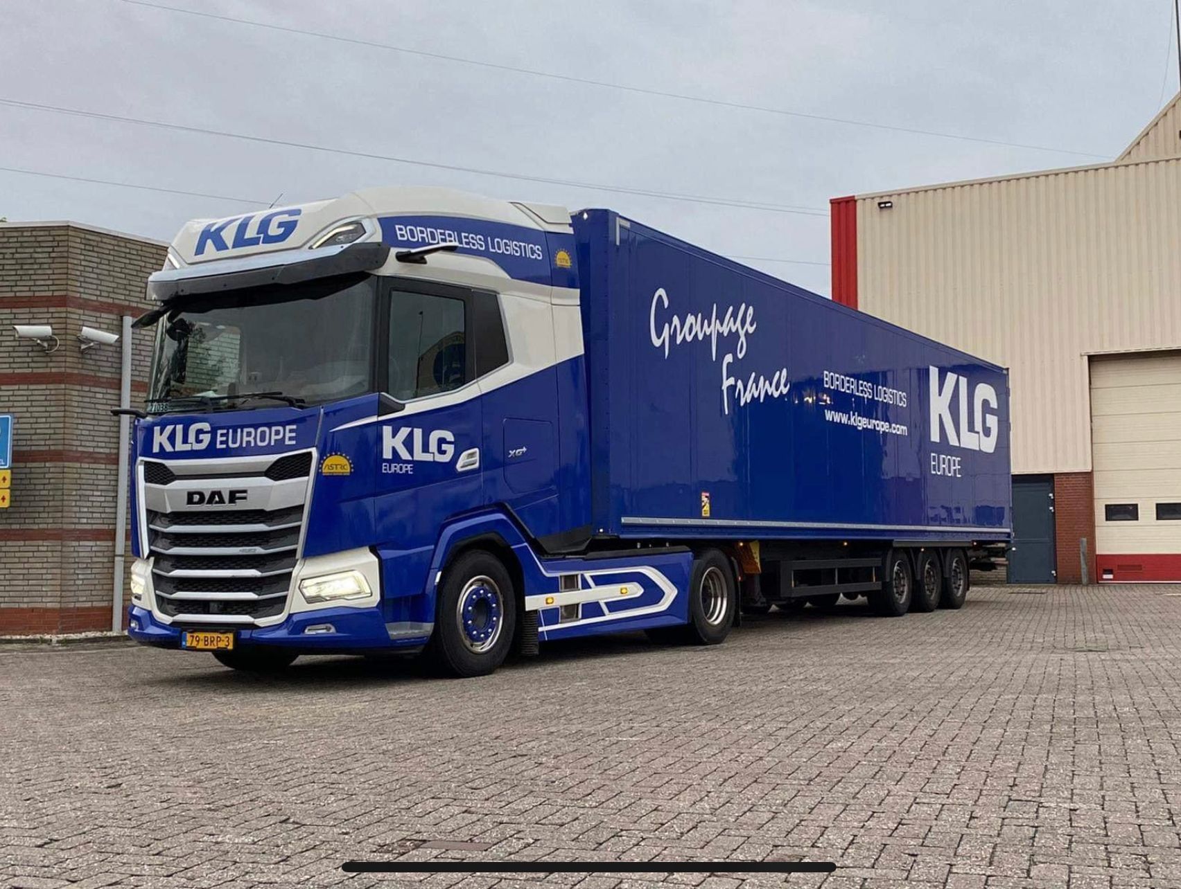 Een blauw-witte vrachtwagen staat geparkeerd voor een gebouw.
