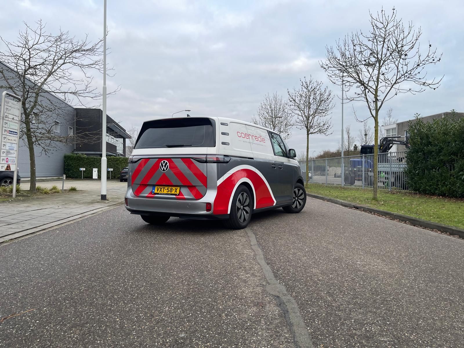 Een grijs-witte bestelwagen met rode geometrische stickers en veiligheidsstrepen op de achterkant.