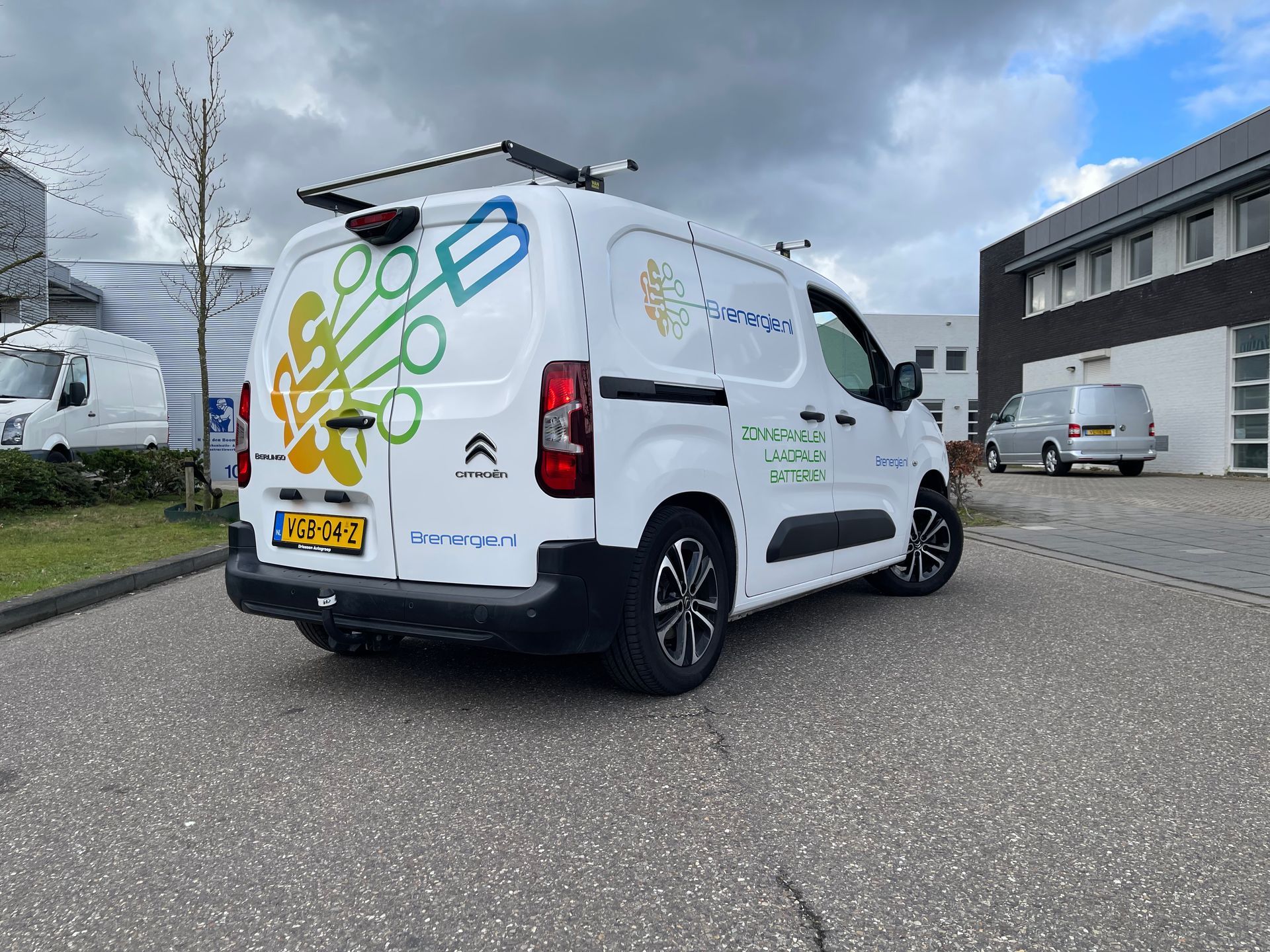 Een wit busje staat geparkeerd voor een gebouw.