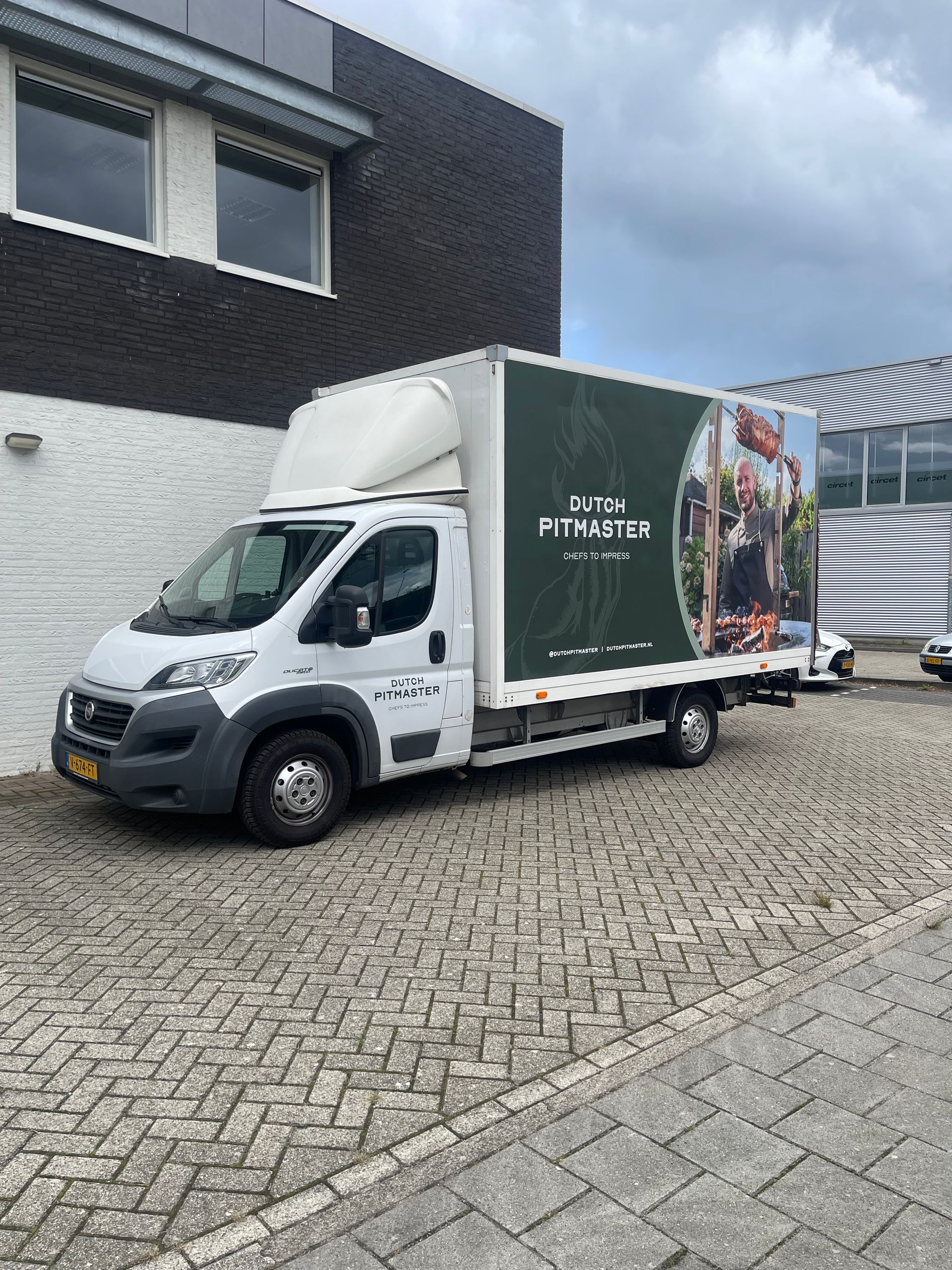 Een wit busje staat geparkeerd voor een gebouw.