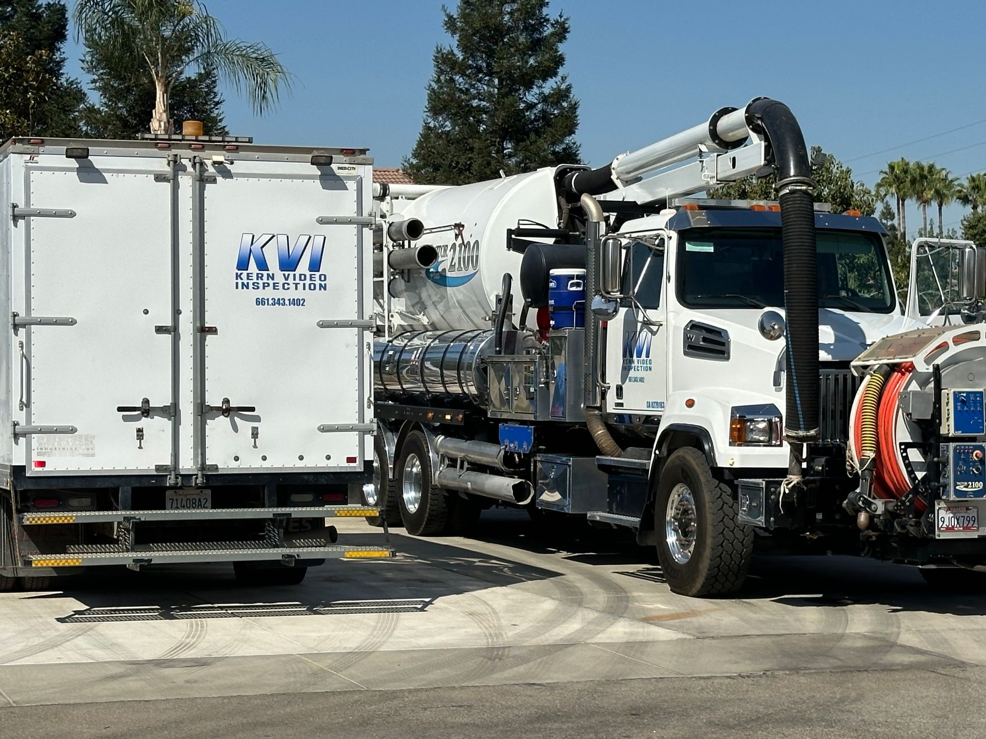 Two white trucks, side by side with the word KVI on the side and rear of the vehicles