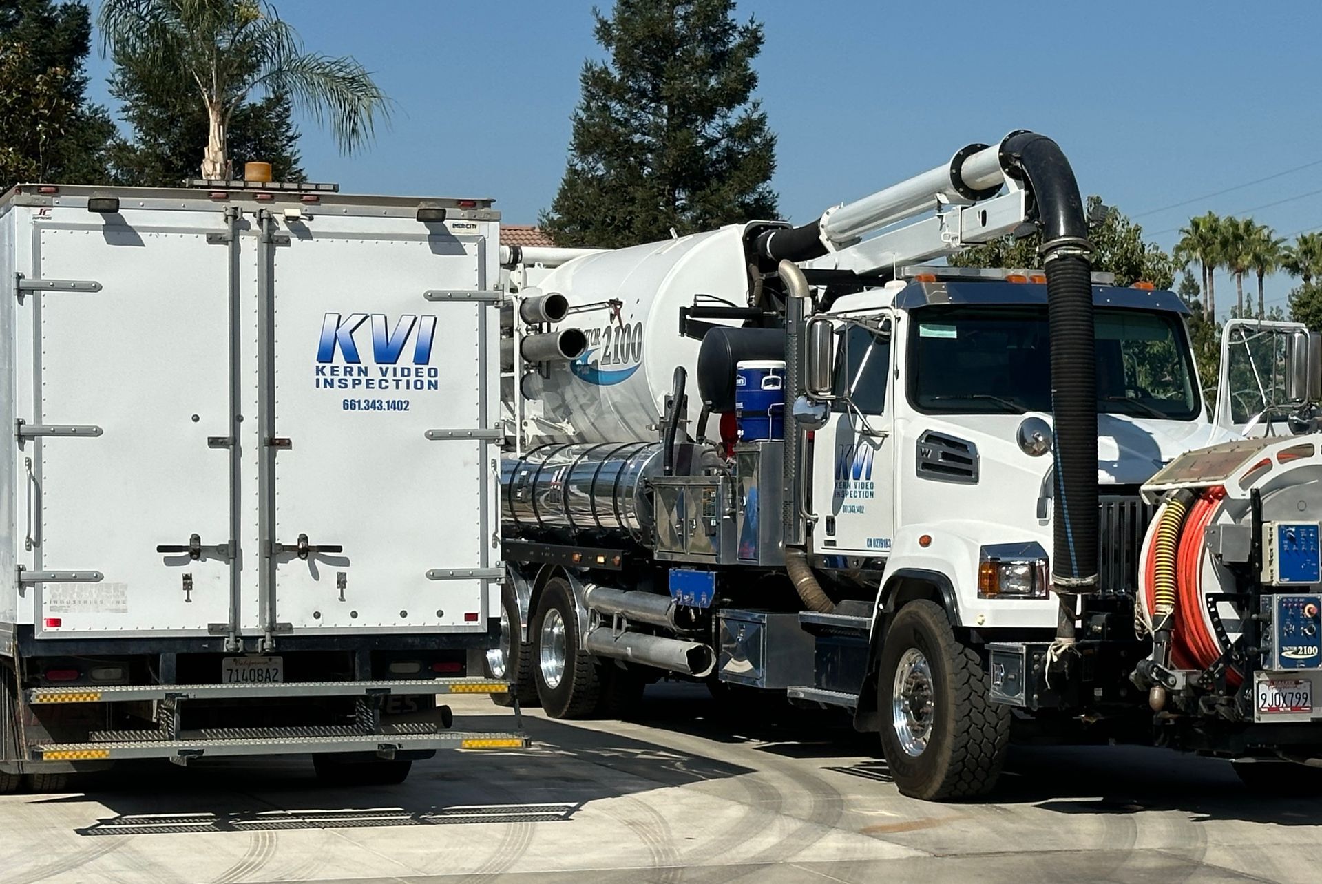 Two white trucks, side by side with the word KVI on the side and rear of the vehicles