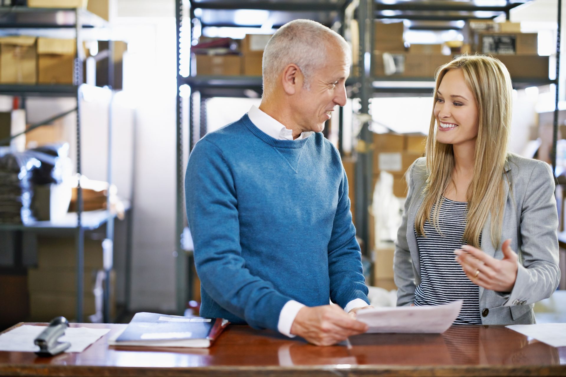 Two people in a workshop reviewing papers and talking across a workbench.